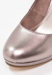 Gros plan d'une chaussure fermée rose clair métallisée avec une texture en cuir lisse et une doublure intérieure marron douce.