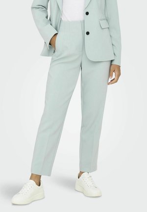 Pantalones ajustados de color verde claro, confeccionados en una tela suave, con cintura alta, piernas rectas y bolsillos laterales. Combinados con zapatillas blancas.
