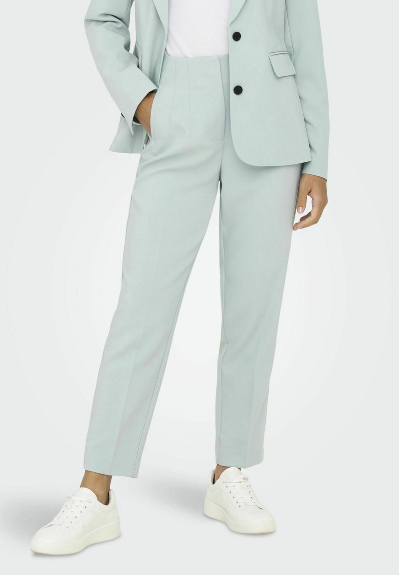 Pantalones ajustados de color verde claro, confeccionados en una tela suave, con cintura alta, piernas rectas y bolsillos laterales. Combinados con zapatillas blancas.