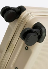 Tvrdý kufr s texturovaným béžovým povrchem, černými kolečky a robustními prvky. Kolečka jsou navržena pro hladkou mobilitu.