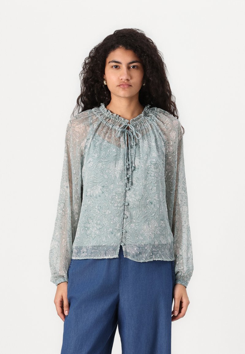 Hellem blaues, blumengesäumtes Bluse mit gerafftem Ausschnitt, Knopfleiste und durchsichtigen langen Ärmeln. Weicher, fließender Stoff mit leichter Textur.