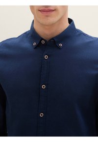 Camisa de color azul marino con botones, confeccionada en una tela texturizada, que presenta un cuello con solapa y botones de madera clara en la parte delantera.