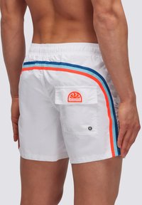Pantaloni da bagno bianchi con strisce laterali blu e arancioni, vita elastica, tasca posteriore, e logo circolare. Tessuto liscio e leggero.