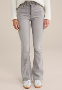 Helle graue, ausgestellte Jeans mit hohem Bund, die über dezente Waschungen und Taschen vorne verfügt, kombiniert mit weißen Sneakers.