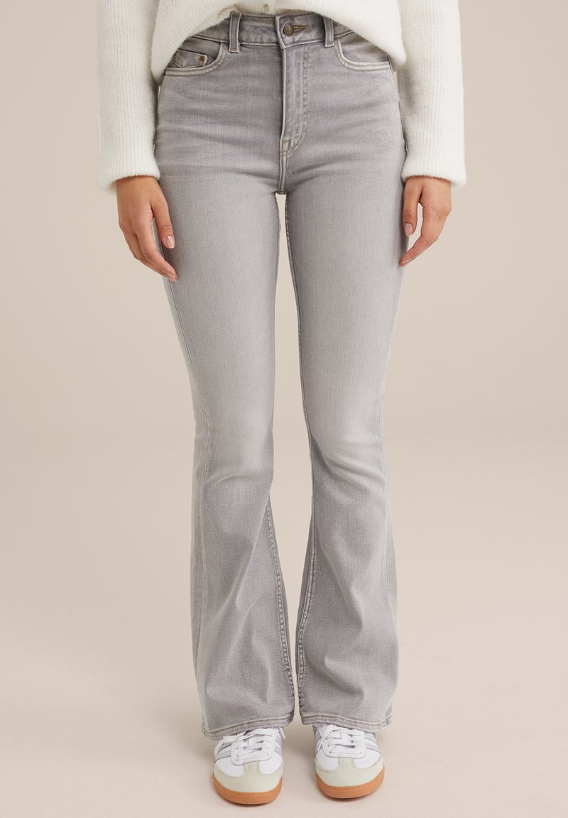 Helle graue, ausgestellte Jeans mit hohem Bund, die über dezente Waschungen und Taschen vorne verfügt, kombiniert mit weißen Sneakers.