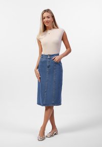 Denim blyantskjørt med høy liv, sidelommer og to frontknapper. Kombinert med en kremfarget ribbestrikket kortermet topp og metalliske sko.