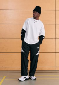 White t-shirt with black sleeves featuring stars, paired with black pants sporting three white stripes and Adidas logo, complemented by black sneakers.