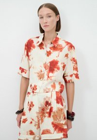 Linnen kortekoo-shirt met een rood en oranje bloemenpatroon op een crèmekleurige achtergrond, met een kraag en knoopsluiting.