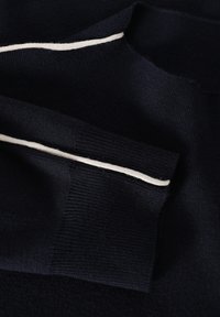 Maglione lavorato a maglia blu navy con una texture morbida e una striscia bianca a contrasto lungo il colletto. Il tessuto appare spesso e accogliente.