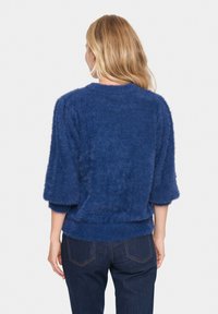 Mörkblå fluffig tröja med trekvartsärmar och rund hals. Har en mjuk, texturerad yta och en figursydd midja.