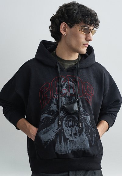 Zwarte hoodie met rood "GCDS" logo, grafisch ontwerp met een skelet, gestructureerd materiaal, oversized pasvorm en zwarte buidel met bandjes.