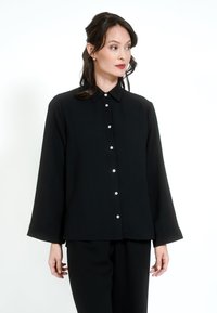 Black long-sleeve shirt with a collar, featuring front button closure and a loose fit. Smooth texture, minimalistic design, and no prominent patterns.