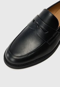 Black leather loafers feature a raised detail on the vamp, rounded toe, and a stitched sole for added durability.