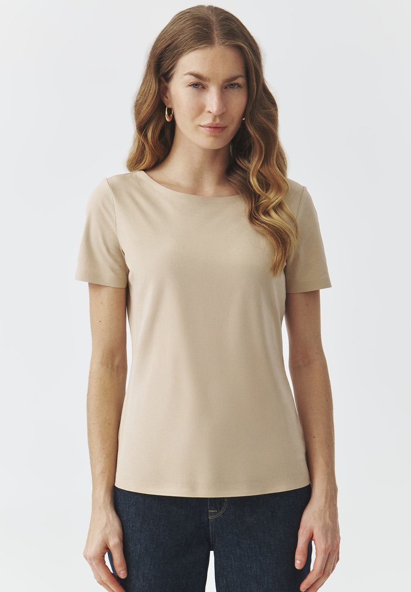 Camiseta de manga corta beige con cuello redondo, hecha de una tela suave, que presenta una textura lisa y un diseño ajustado. Combinada con jeans oscuros.