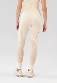 Leggings beige a vita alta con pannelli in rete, caratterizzati da dettagli ritagliati lungo i lati e un design aderente. Abbinati a sneakers chiare.