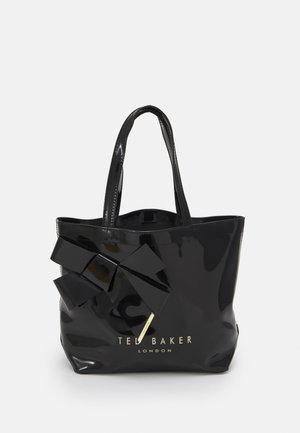 Czarna błyszcząca torba typu tote z dużą ozdobną kokardą i złotym logo "Ted Baker London" z przodu, wyposażona w dwa paski na ramię.
