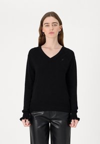 Schwarzer V-Ausschnitt-Pullover aus weichem Strickstoff, mit gerippten Bündchen mit gezacktem Rand und einem kleinen Logo-Emblem auf der Brust.