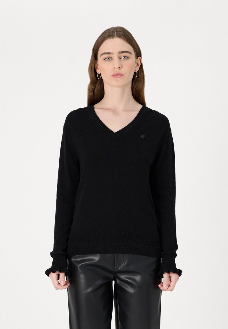 Schwarzer V-Ausschnitt-Pullover aus weichem Strickstoff, mit gerippten Bündchen mit gezacktem Rand und einem kleinen Logo-Emblem auf der Brust.