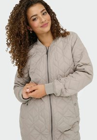 Quiltet beige bomberjakke med lynlås, ribbede manchetter, to sidelommer og et diamant mønster hele vejen igennem.