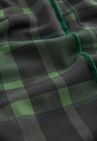 Tissu à carreaux noir et vert avec un motif texturé et une finition lisse, souligné de coutures vertes le long des bords.