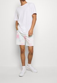 T-shirt en coton blanc associé à un short tie-dye pastel clair avec un ourlet effiloché, porté avec des baskets blanches et des chaussettes de cheville.