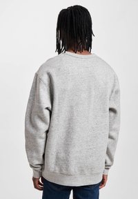 Felpa grigia con collo rotondo realizzata in un tessuto texturizzato, con polsini e orlo a coste. Presenta spalle ribassate e una vestibilità rilassata, indossata con jeans blu.