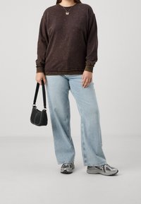 Felpa marrone a maniche lunghe con un design sbiadito, abbinata a jeans a zampa d'elefante di un blu chiaro. Gli accessori includono una borsa nera e sneakers argentate.