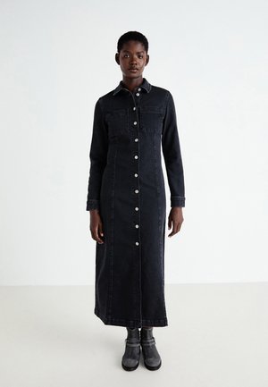 Robe en denim noire longue avec un devant à boutons, deux poches poitrine et un col. La robe a une silhouette ajustée et des manches longues.