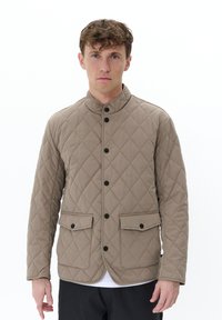 Chaqueta acolchada beige con un alto cuello, botones negros, dos bolsillos frontales y una textura suave. Diseño minimalista y corte ajustado.