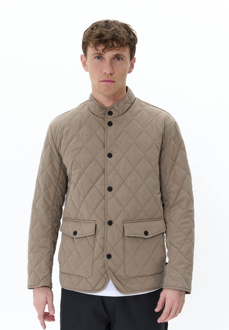 Chaqueta acolchada beige con un alto cuello, botones negros, dos bolsillos frontales y una textura suave. Diseño minimalista y corte ajustado.