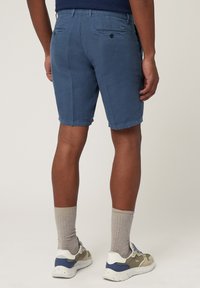 Lichtblauwe shorts van een stof met een gladde textuur, met zij- en achterzakken, en een getailleerde pasvorm. Ggedragen met grijze sokken en sneakers.
