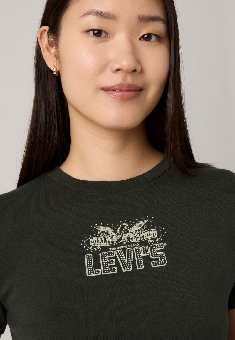 T-shirt ajusté vert foncé en coton, arborant un logo vintage Levi's en crème, avec un col rond et des manches courtes.