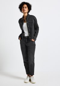 Musta farkkutakki valkoisen paidan päällä, yhdistettynä mustiin farkkuihin ja vaaleisiin lenkkikengiin. Omaa napituskappaleet ja klassisen leikkauksen.