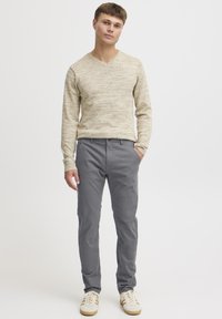 Jersey beige con cuello en V combinado con pantalones grises. El jersey tiene un acabado texturizado, mientras que los pantalones presentan un corte clásico y detalles sutiles en los bolsillos.