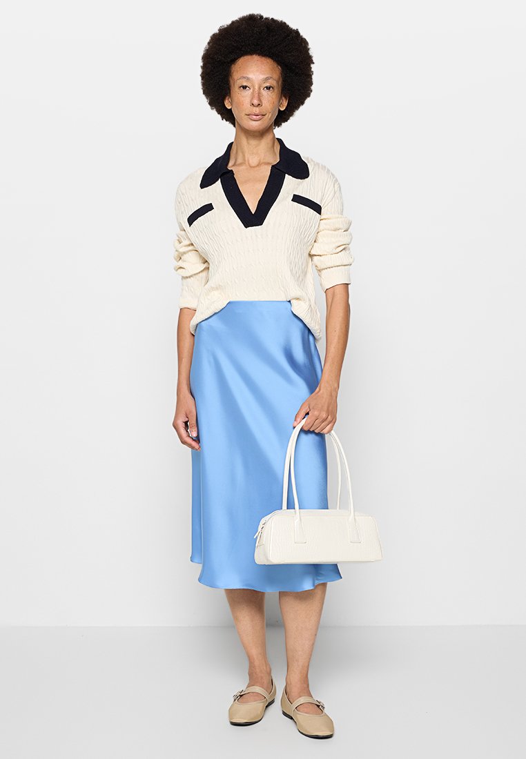 Maglione a treccia crema con dettagli blu navy, gonna midi in satin blu, ballerine beige e borsa bianca testurizzata. Completamente elegante ed essenziale.