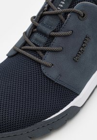 Navy blue sneaker featuring a textured mesh upper, smooth synthetic accents, and grey laces. Rubber sole with tread pattern for traction.