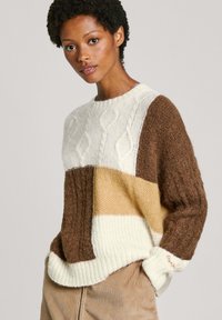 Adīta džemperis ar krāsu blokiem brūnā, krēmkrāsas un bežā. Ar teksturētu rakstu un ribotām detaļām piedurknēs un apakšmalā.