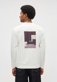 Balta krekla ar gariem piedurknēm, uz muguras atrodas grafisks dizains ar ģeometriskām formām burgundijas, melnā un krēmkrāsā. Gluda kokvilnas tekstūra.