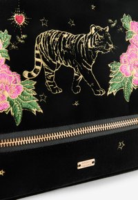 Borsa di tessuto nera con ricami dorati di una tigre e design floreali rosa, con una cerniera dorata e etichetta del marchio.