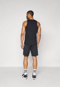 Black tank top, gray shorts with pockets, black and white striped socks, and black sneakers. Model shown from the back.