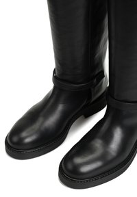 Czarne skórzane botki za kolano o gładkiej fakturze, zaokrąglonym nosku, minimalistycznym designie i płaskiej podeszwie. Regulowany pasek przy kostce.