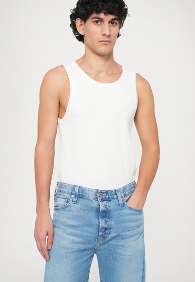 Valge puuvillane top, ümmarguse kaelusega, kantud helesiniste teksadega, millel on kerge kulumine, taskud ja klassikaline lõige.