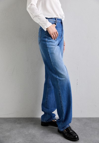 Light blue denim wide-leg jeans with a high waist, featuring prominent stitching and a slightly faded texture. Paired with black shoes.