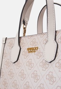 Cremefarvet mønstrede håndtaske med guldbeslag. Har en struktureret design, dobbelte håndtag og sort kant rundt om de øverste kanter.