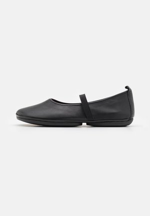 Ballerines en cuir noir avec un bout arrondi, une sangle élastique sur le cou-de-pied et une semelle à profil bas. Texture lisse et design minimaliste.