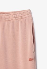 Pantalons de survêtement rose clair avec une taille élastique, des poches latérales et une finition texturée. Présente un logo brodé discret sur la jambe inférieure.