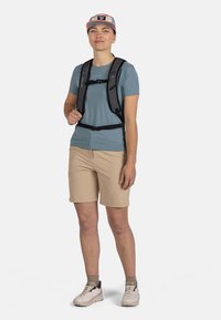Černý batoh s nastavitelnými popruhy přes tyrkysové tričko. Světle béžové šortky a světlá obuv kompletuje volnočasový outfit.
