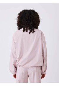 Chaqueta rosa claro extragrande con mangas largas, puños fruncidos y textura suave, vista desde atrás. Combinada con pantalones a juego.