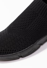 Crne slip-on cipele s teksturiranim pletenim gornjim dijelom s ventilacijskim rupama i fleksibilnim crnim gumenim đonom. Glatka površina s rebrastim gležnjem.