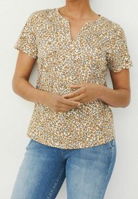 Bluzka z krótkimi rękawami w brązowo-białym kwiatowym wzorze, z dekoltem w kształcie litery V i luźnym krojem, zestawiona z jasnoniebieskimi dżinsami.